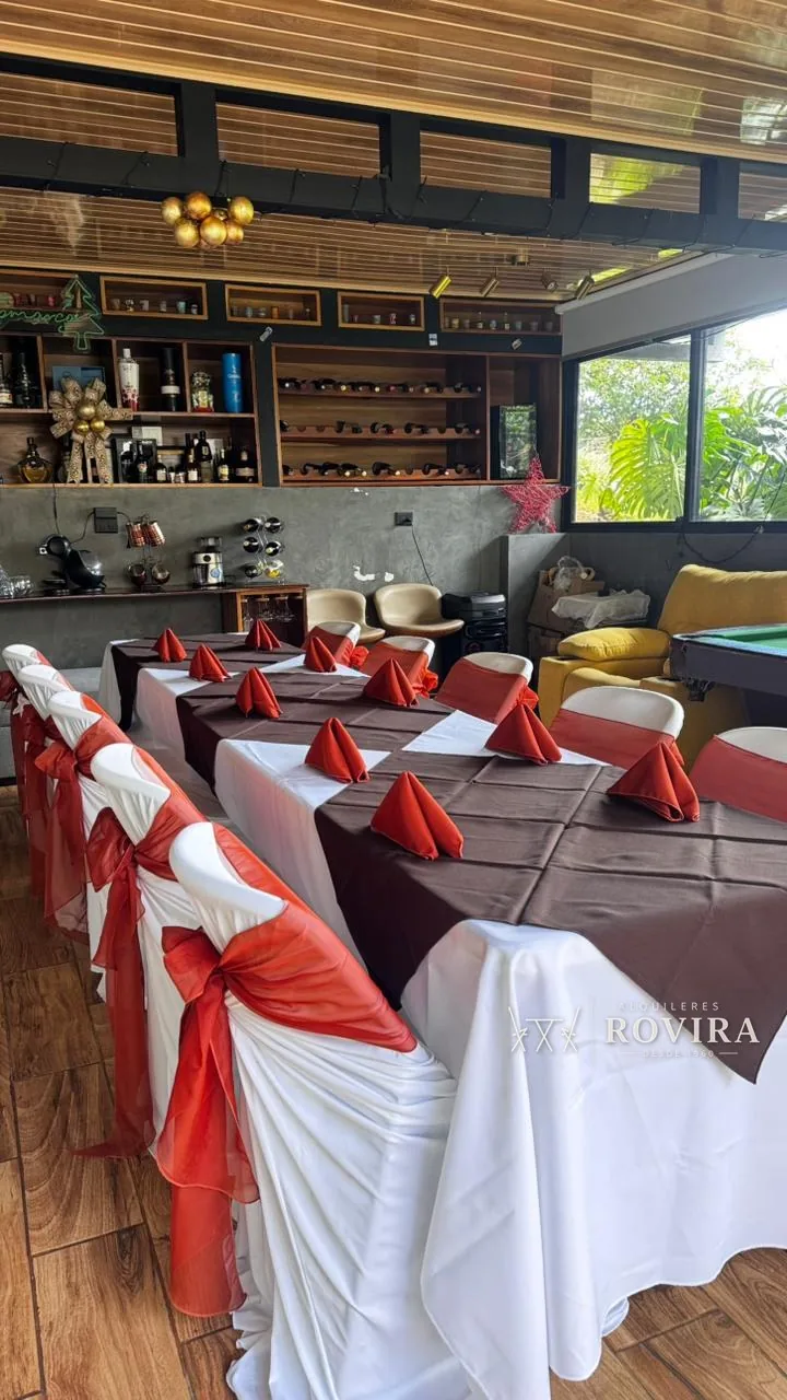 Mesa vestida en blanco con camino café y servilletas rojas dobladas, ambiente de bar acogedor