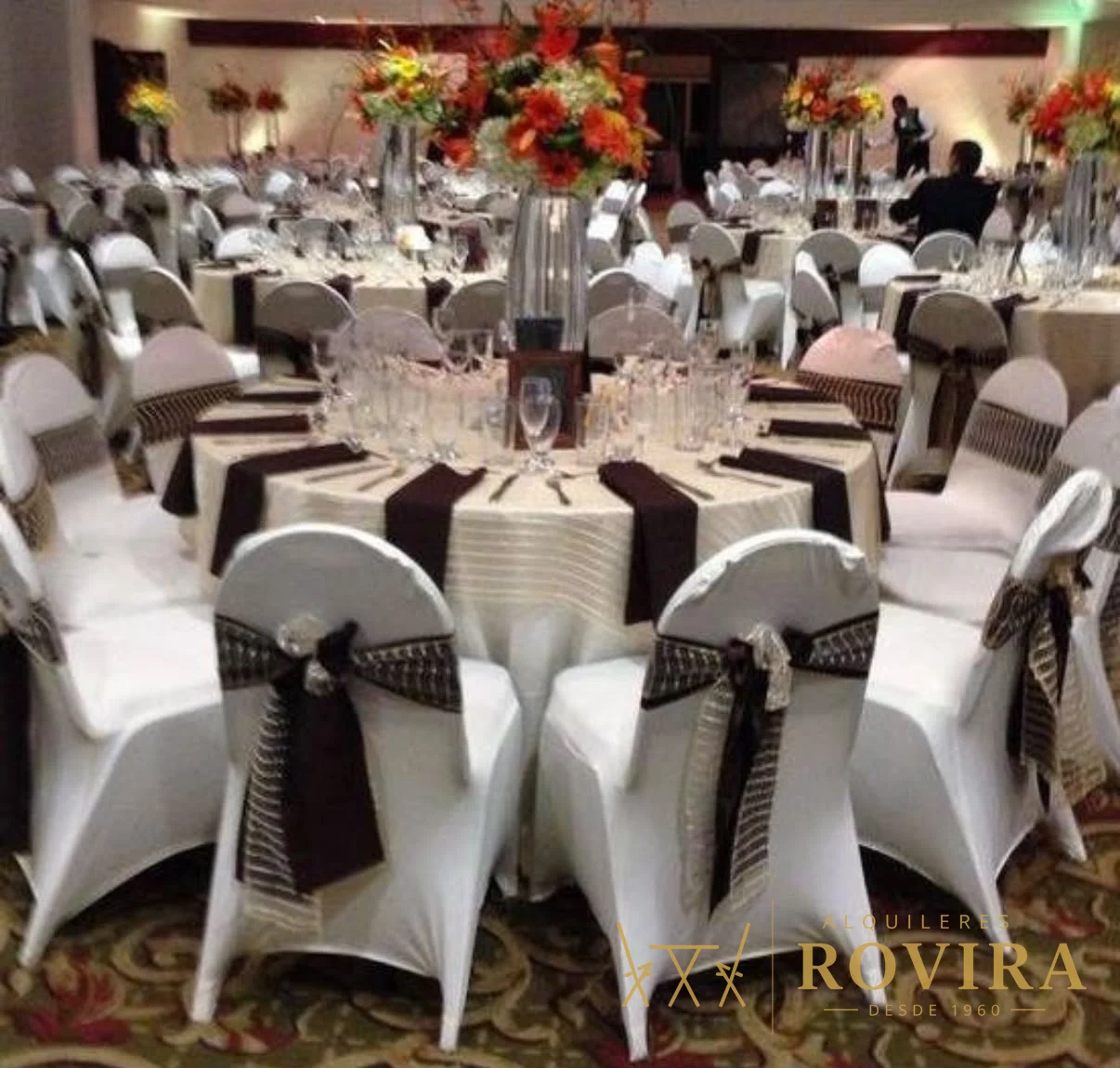 Salón elegante con manteles blancos, caminos y lazos color chocolate y centros florales altos