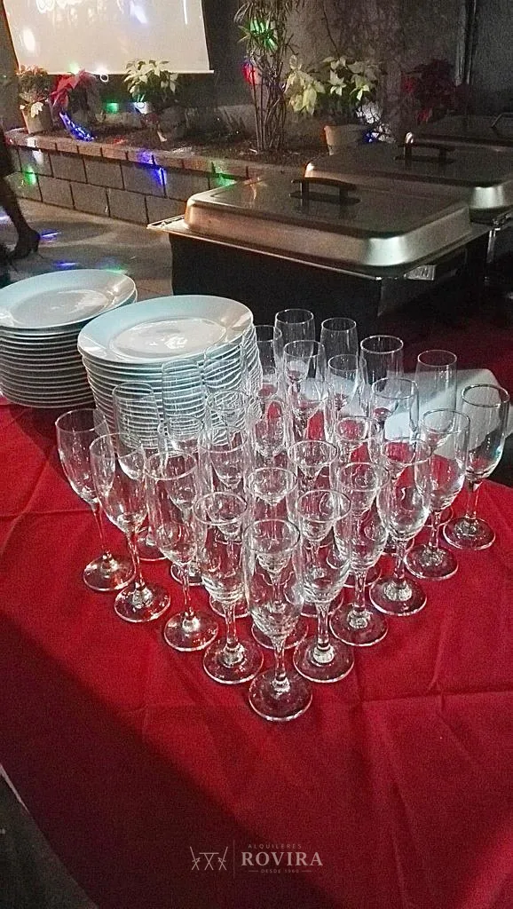 Copas de vidrio apiladas junto a hielera de acero, cristalería y equipo de bebidas