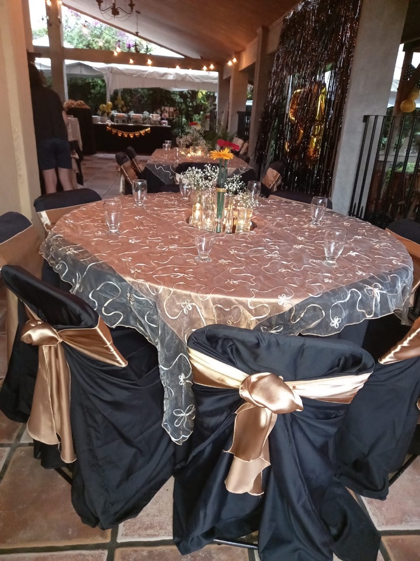 Mesa redonda vestida en dorado y negro con overlay de organza, sillas negras con lazo dorado