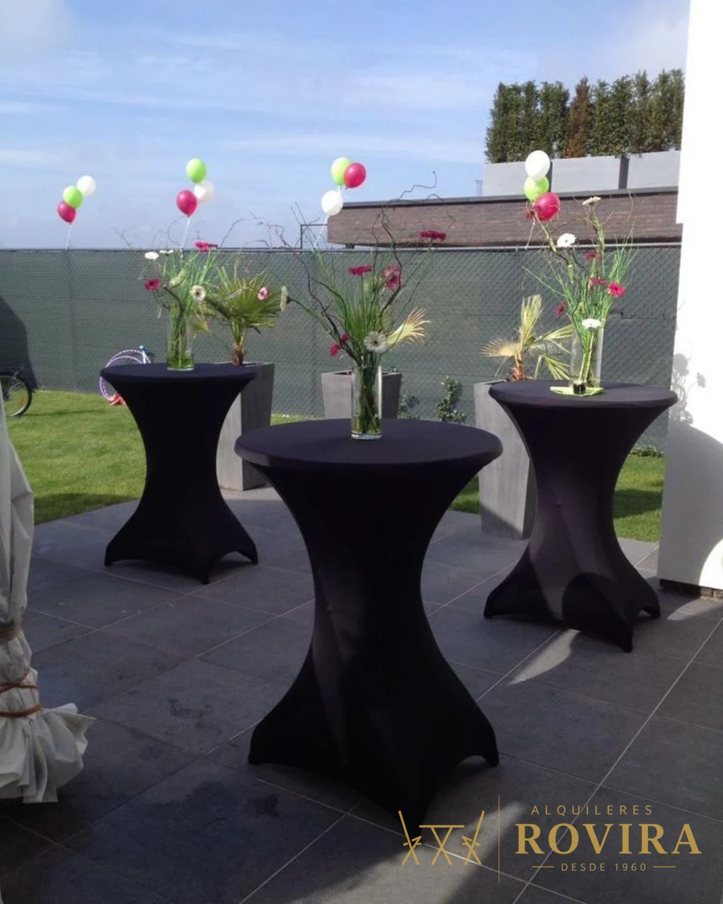 Mesas cocktaileras altas con forro negro y centros florales, evento en exterior
