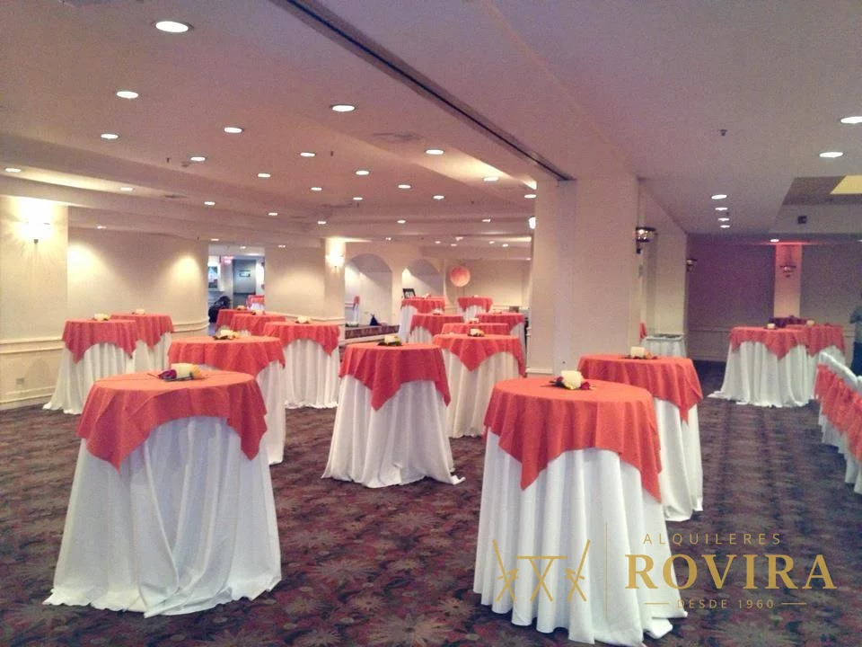 Mesas cocktaileras altas con forro blanco y overlay coral, montaje amplio en salón