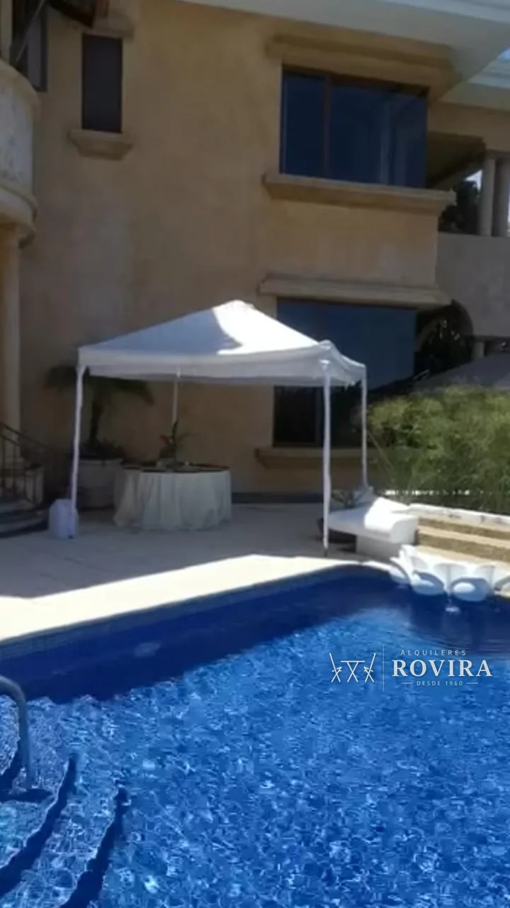 Toldo blanco junto a una piscina en una casa de lujo, mesa auxiliar con flores