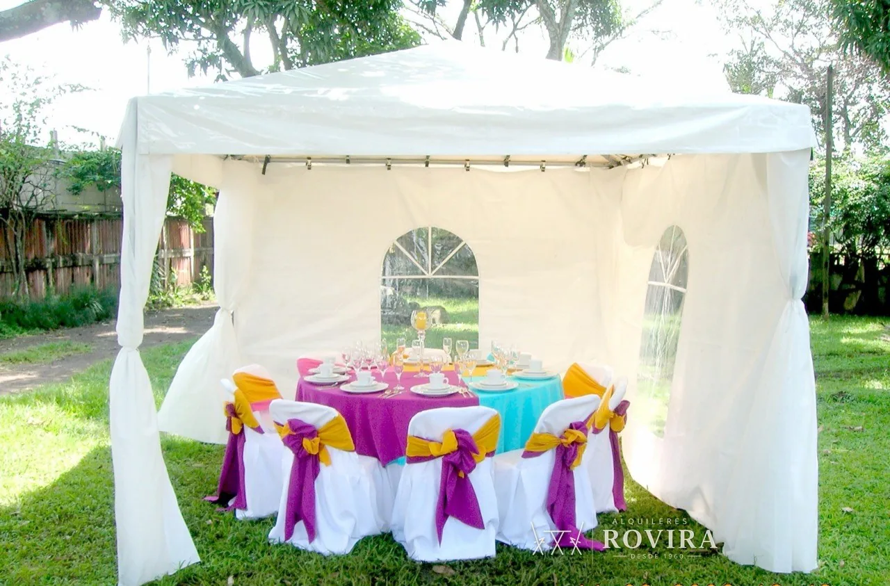 Toldo cerrado con paredes laterales y ventanas, mesa redonda vestida en fucsia y turquesa