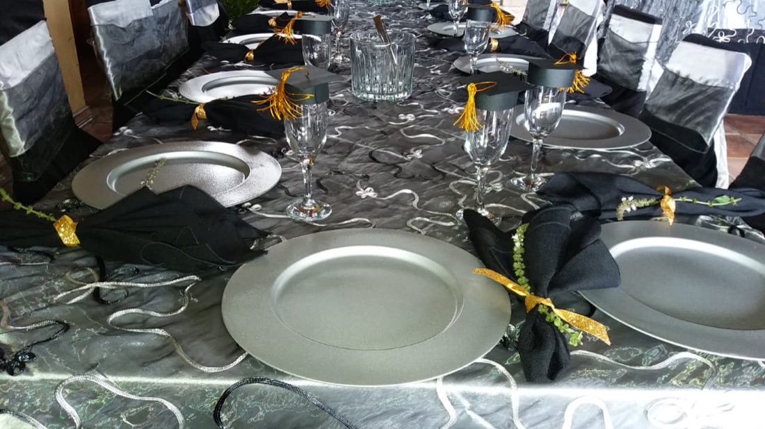 Mesa de graduación con mantel plateado y negro, platos base plateados, copas de champagne