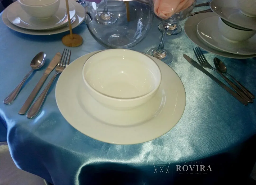 Puesto de mesa con bowl blanco y cubiertos sobre mantel azul satinado
