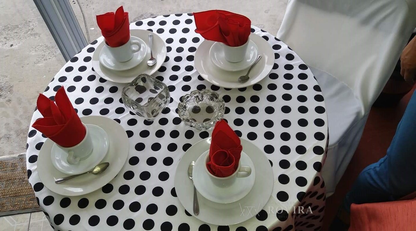 Mesa redonda con mantel de lunares blanco y negro, tazas de café y servilletas con rosa roja