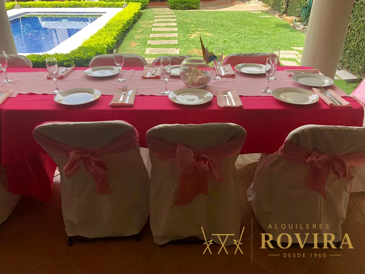 Baby shower de niña con mantel fucsia y forros de silla con lazo rosado, junto a la piscina