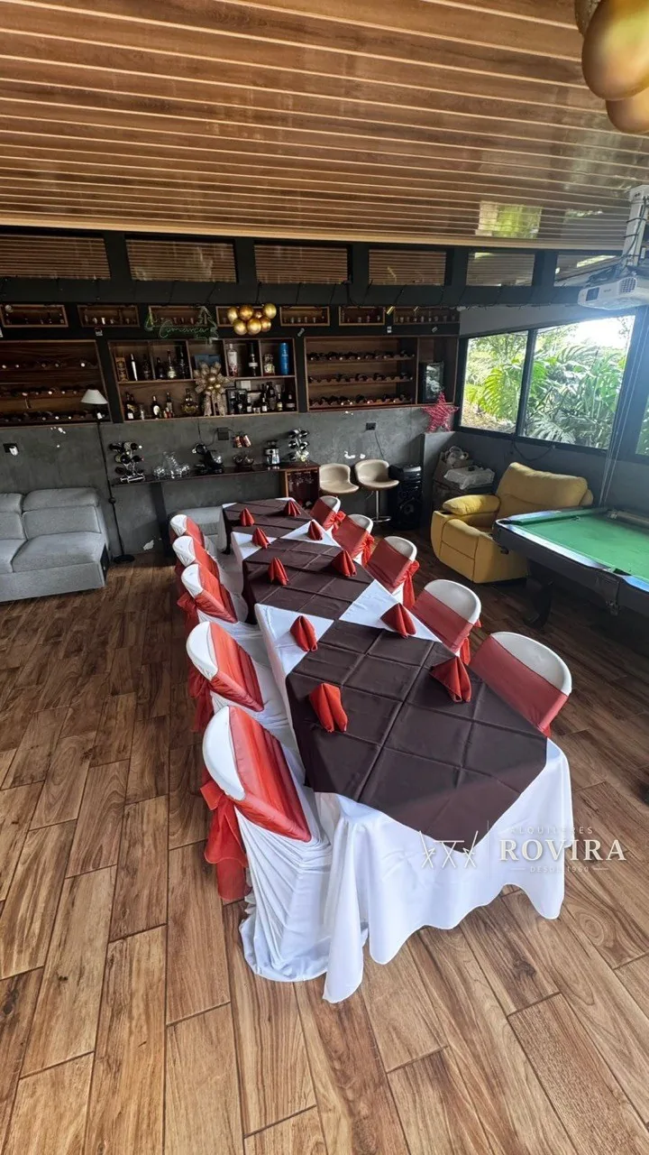Mesas vestidas en café con lazo rojo y servilletas rojas, en sala de juegos con bar y mesa de billar