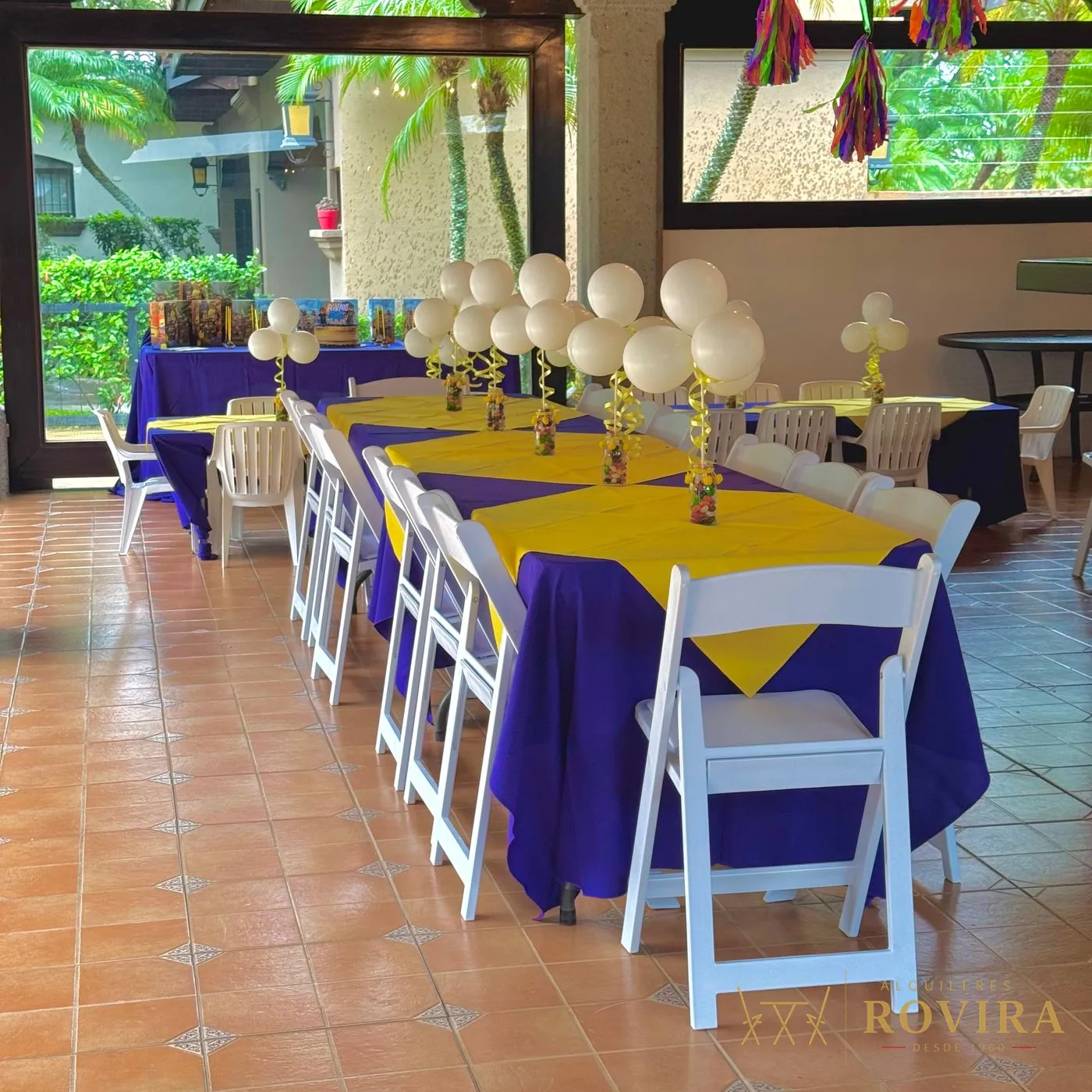 Mesas rectangulares vestidas en morado con camino amarillo y sillas plegables blancas acojinadas, fiesta infantil en rancho con vista al jardín
