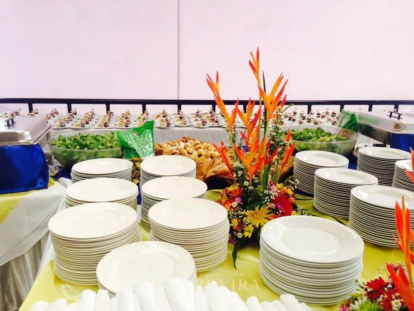 Buffet montado con torres de platos y arreglo floral tropical, servicio de catering