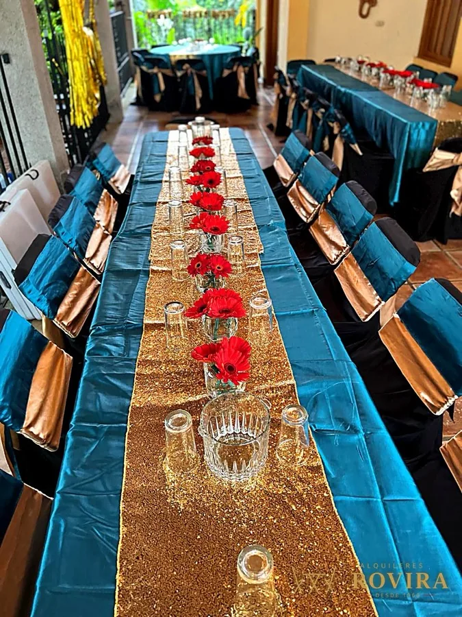 Mesa larga en turquesa con camino dorado y pétalos de rosa