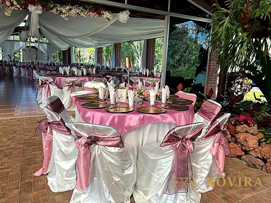 Mesa principal de boda con mantel rosa, platos base dorados y arco floral sobre la mesa