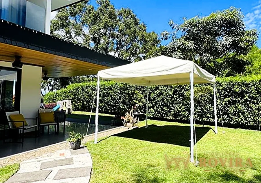 Carpa plegable blanca en jardín junto a la casa