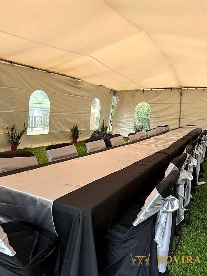Mesa larga bajo toldo con mantel negro y ventanas arqueadas