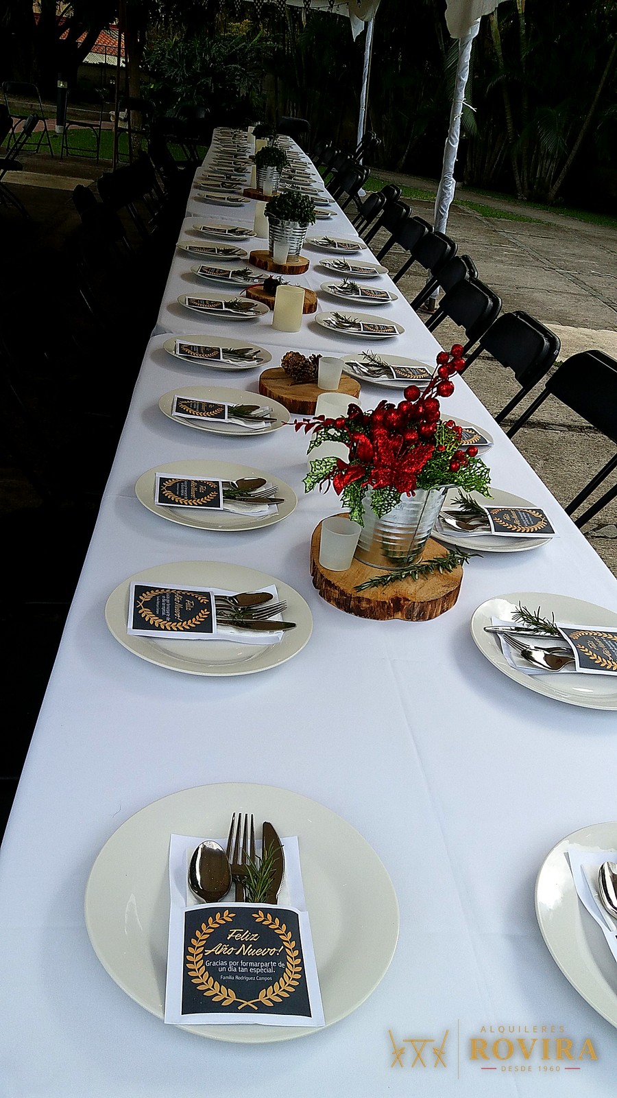 Mesa larga vestida de blanco para una cena de Fin de Año en el patio techado de una casa, con centros de mesa navideños
