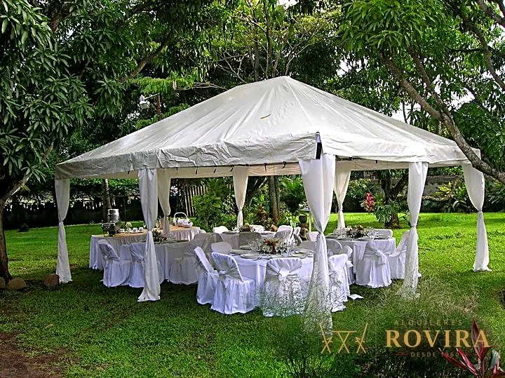 Toldo blanco montado en un jardín, con mesas imperiales vestidas para un evento