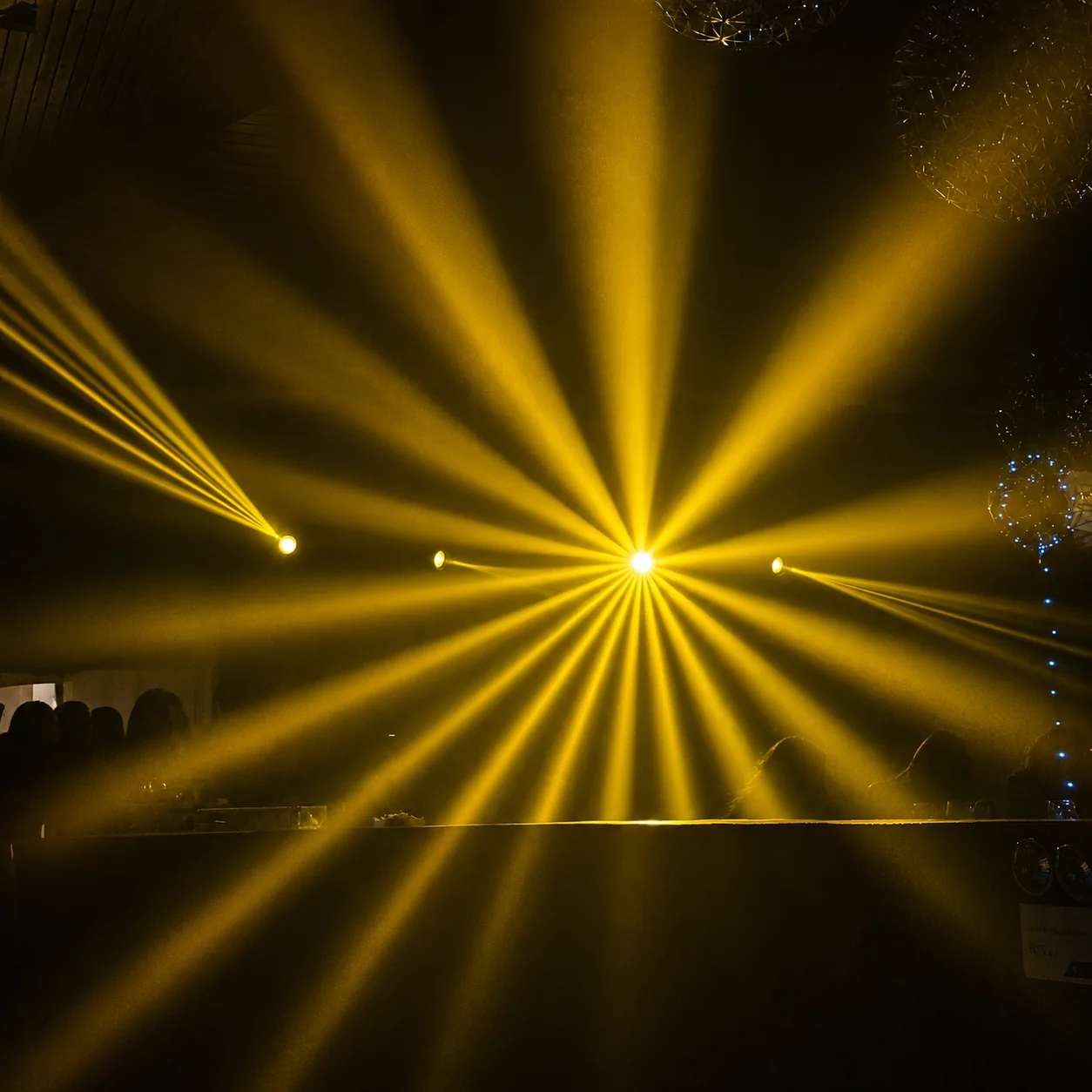 Haces de luz dorados iluminando un salón de evento de noche, producción de iluminación coordinada por Alquileres Rovira